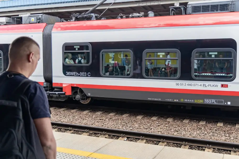 Mężczyzna na peronie obserwujący czerwono-biały pociąg.
