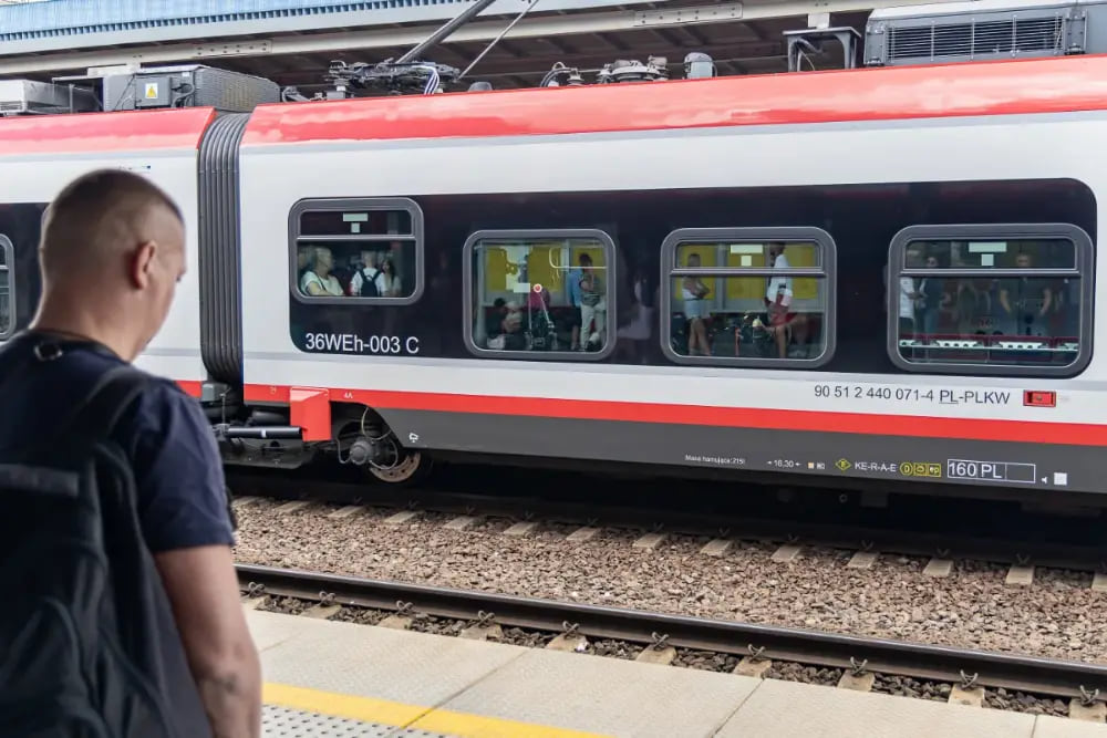 Mężczyzna na peronie obserwujący czerwono-biały pociąg.