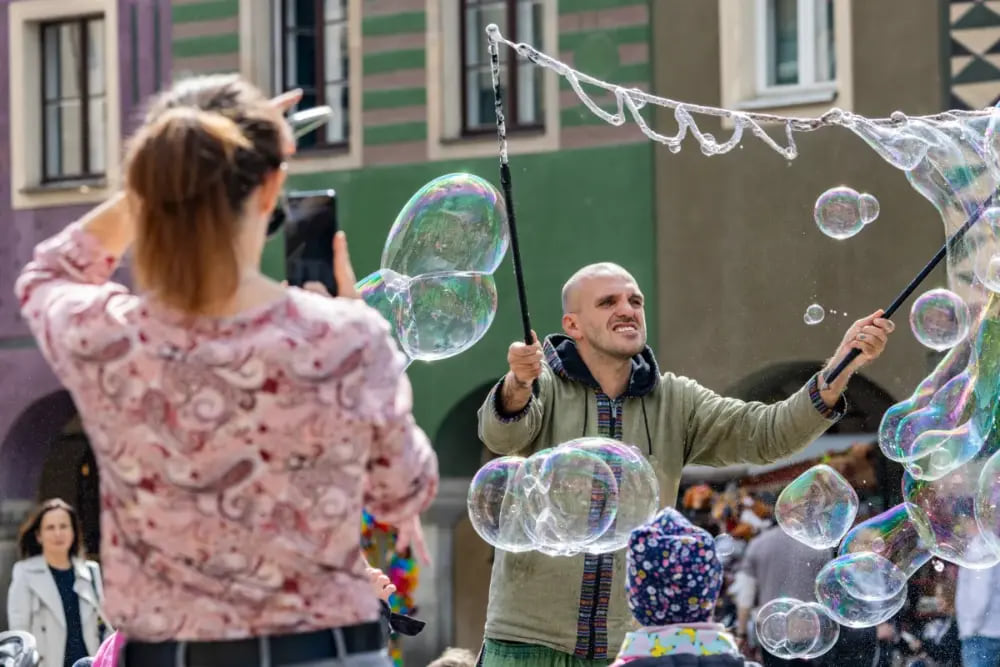 Mężczyzna tworzący wielkie bańki mydlane fotografowane telefonem.