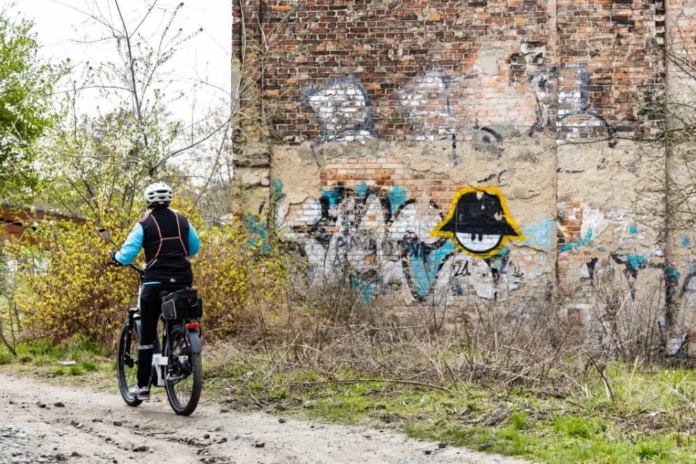 Rowerzysta jadący obok ceglanej ściany pokrytej graffiti.